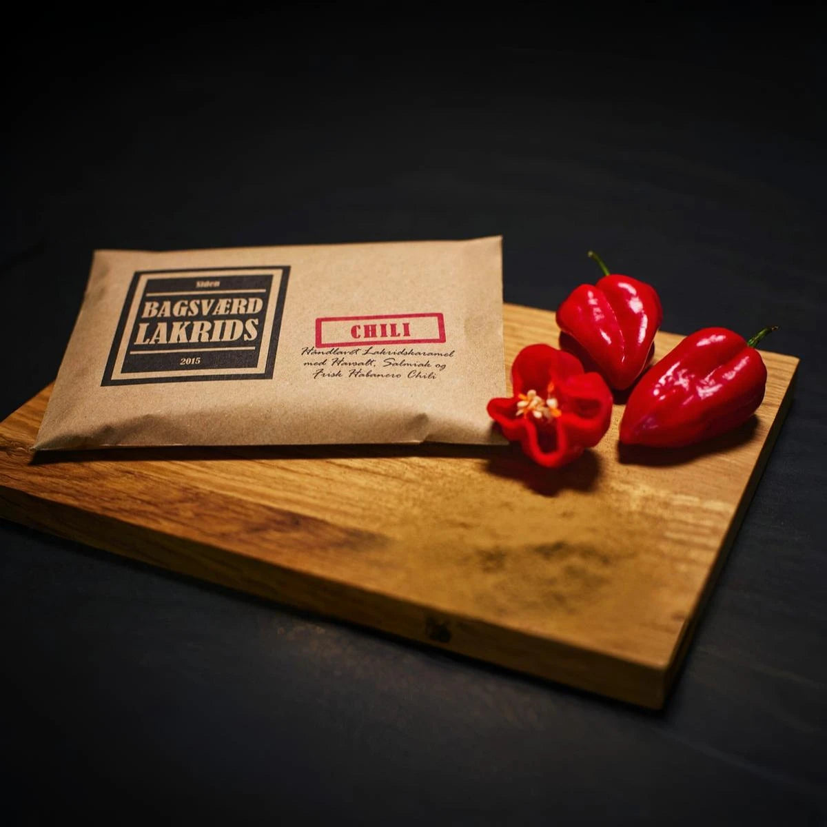 Bagsværd Lakrids Chili 160 g – håndlavet dansk lakridskaramel med habanero chili - Her vist på et træ skærebræt med tre habanero chillier