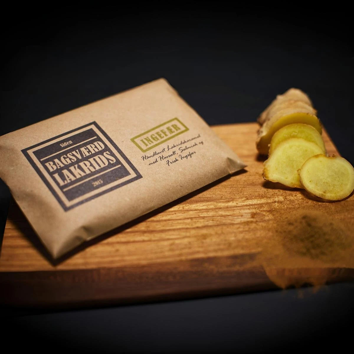 Bagsværd Lakrids Ingefær 160 g – håndlavet dansk lakrids med frisk ingefær og krydret smag - Her præsenteret på et træskærebræt sammen med udskåret ingefær