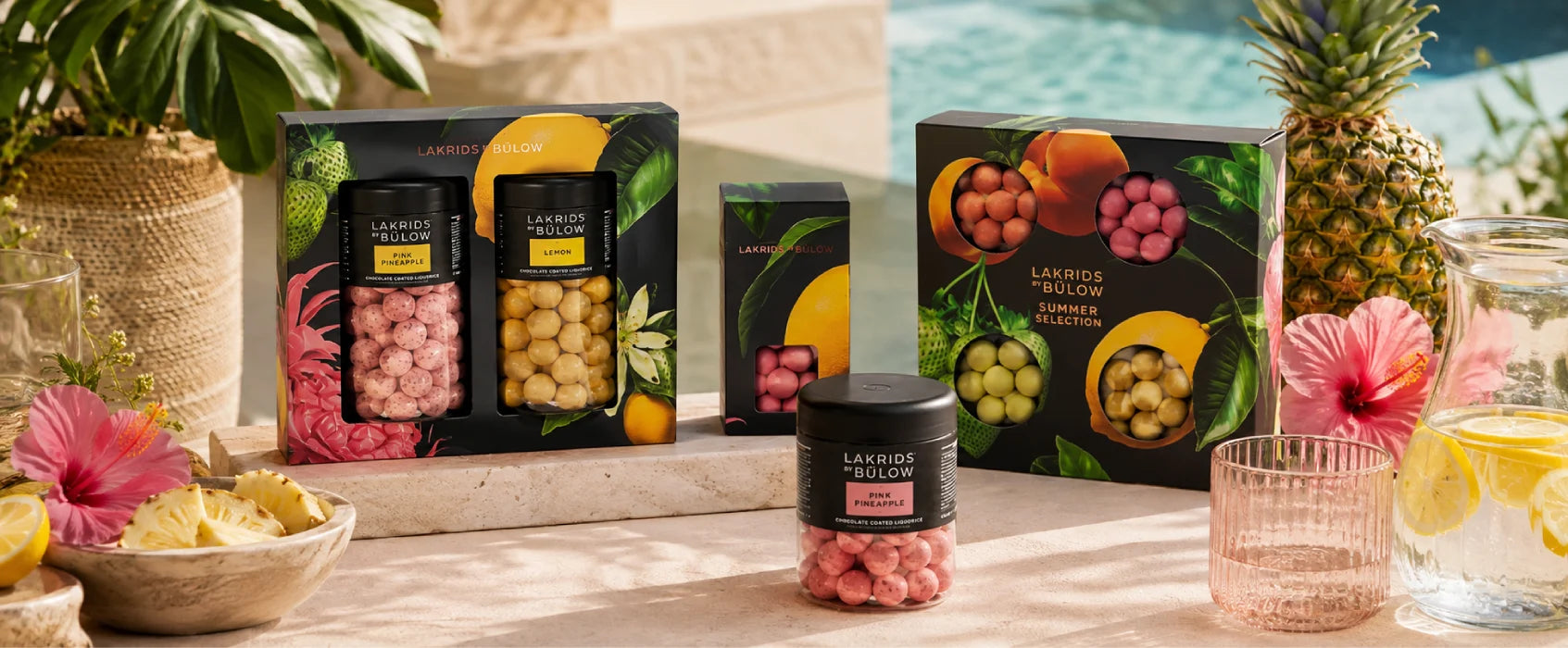 Lakrids by Bülow sommerkollektion med Pink Pineapple, Lemon og Summer Selection i tropiske omgivelser med ananas, blomster og lemonade.
