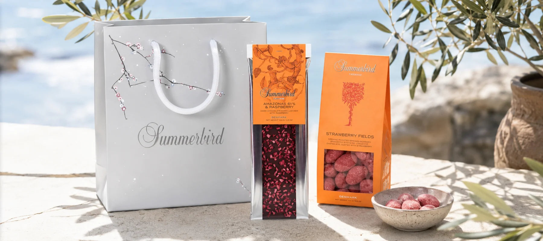 Summerbird chokolade med Amazonas 61% & Raspberry og Strawberry Fields i sommerlige omgivelser med gavepose, olivengrene og havudsigt.