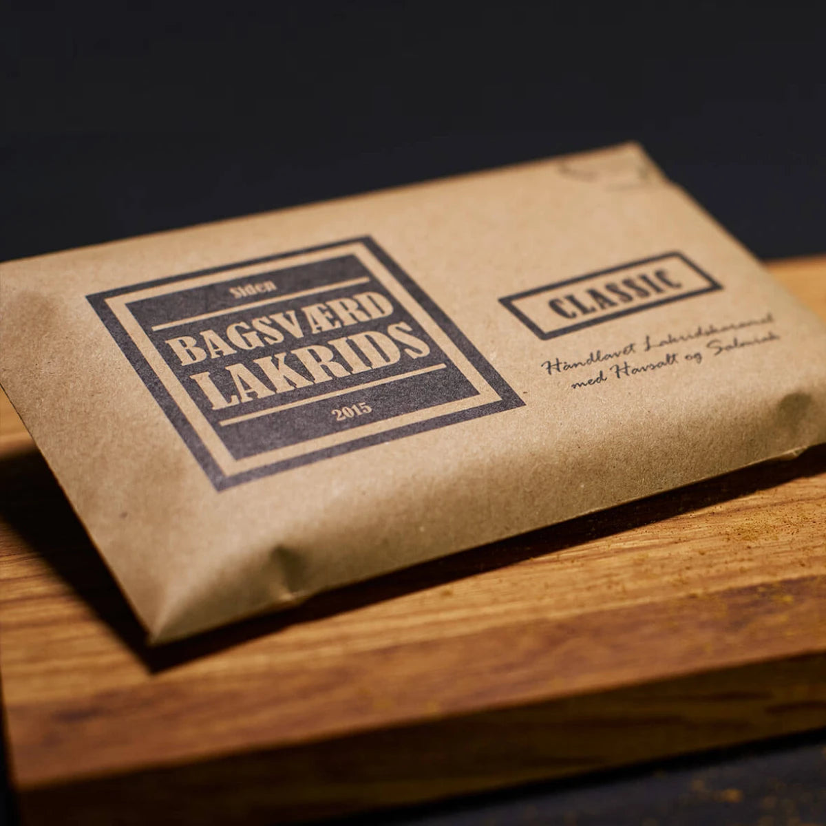 Bagsværd Lakrids Classic 160 g – håndlavet dansk lakridskaramel med salt og salmiak - Her præsenteret på et træskærebræt med lidt lakridsstøv nederst til højre