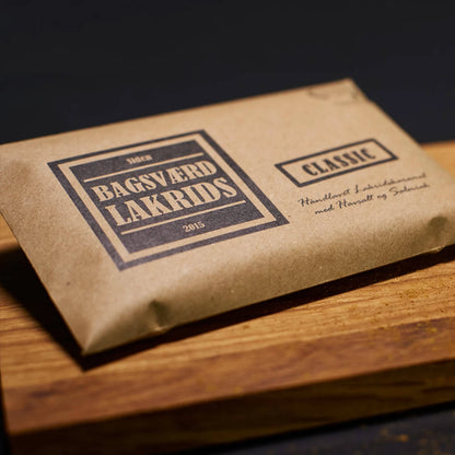 Bagsværd Lakrids Classic 160 g – håndlavet dansk lakridskaramel med salt og salmiak - Her præsenteret på et træskærebræt med lidt lakridsstøv nederst til højre