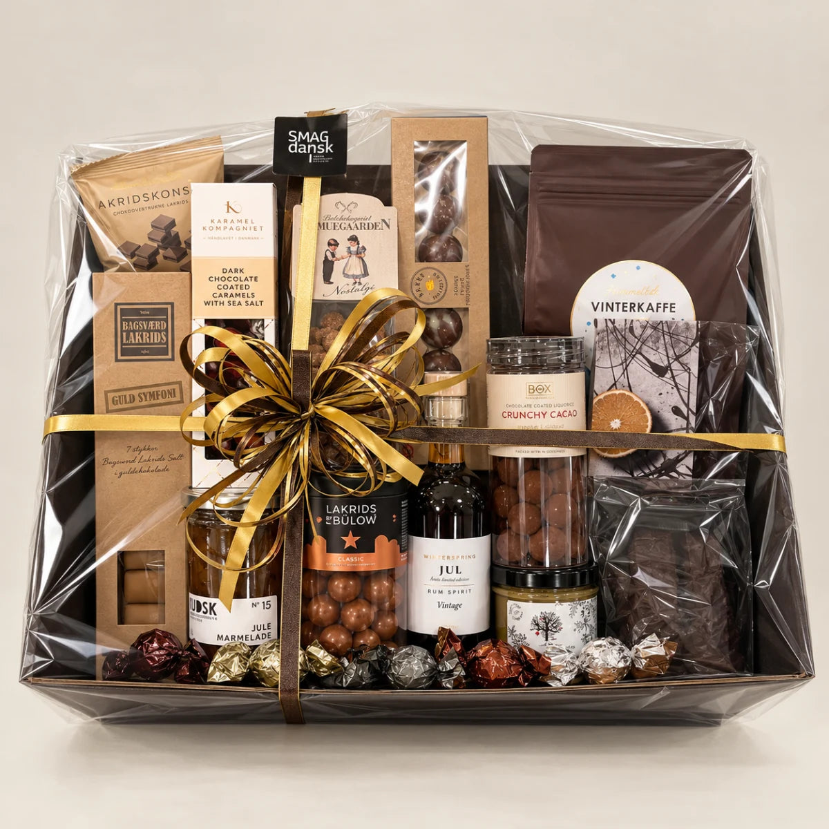 Eksklusiv julegavekurv fra SMAGdansk med dansk lakrids, chokolade, karameller, vinterkaffe, julemarmelade og julespiritus, indpakket i cellofan med guldbånd.