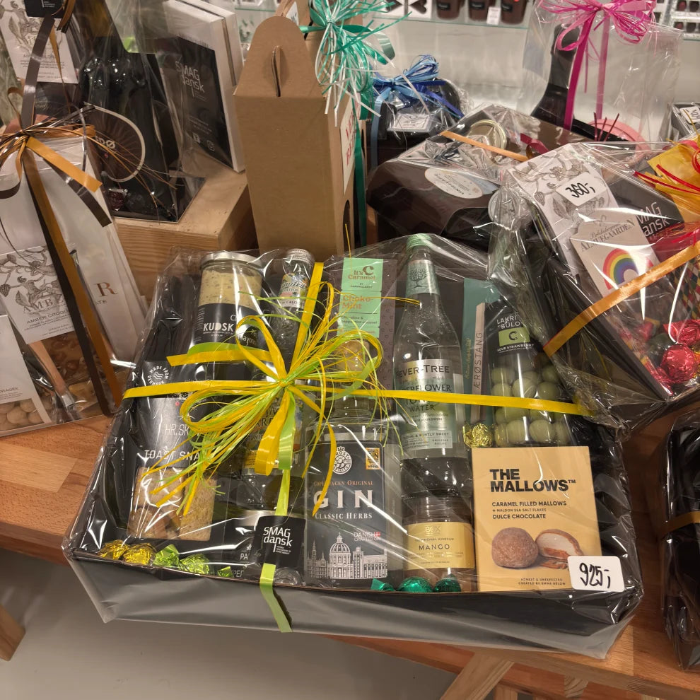 SMAGdansk gavekurve med danske delikatesser – stor gavekurv fyldt med gin, tonic, chokolade, lakrids og snacks, flot indpakket i cellofan med gult bånd, ideel som firmagave, værtindegave eller fødselsdagsgave.