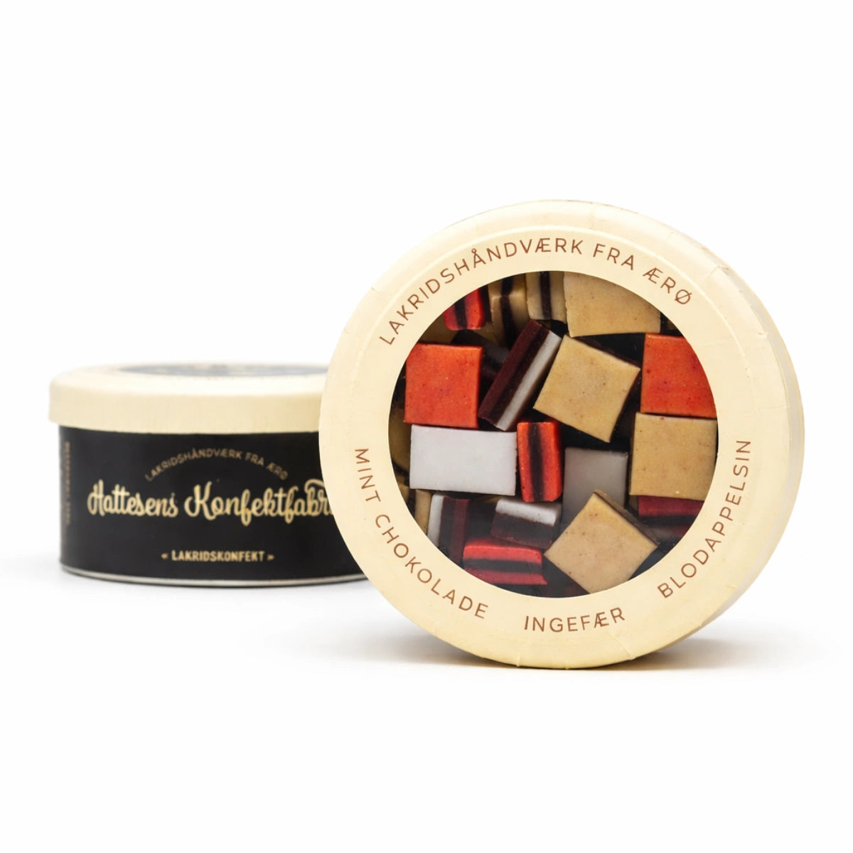 To runde æsker med Hattesens Konfektfabrik lakridskonfekt med gennemsigtigt låg og sort etiket, fyldt med håndlavede lakridsstykker i smagsvarianter som mintchokolade, ingefær og blodappelsin – dansk gourmetlakrids i gavevenlig indpakning.