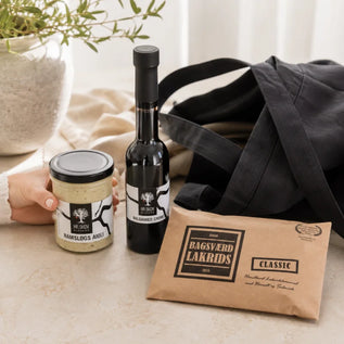 SMAGdansk favoritter ved sort stofnet, herunder Bagsværd Lakrids Classic, Hr. Skov Balsamico Creme og Ramsløgs Aioli i et lyst, indbydende delikatesseunivers.